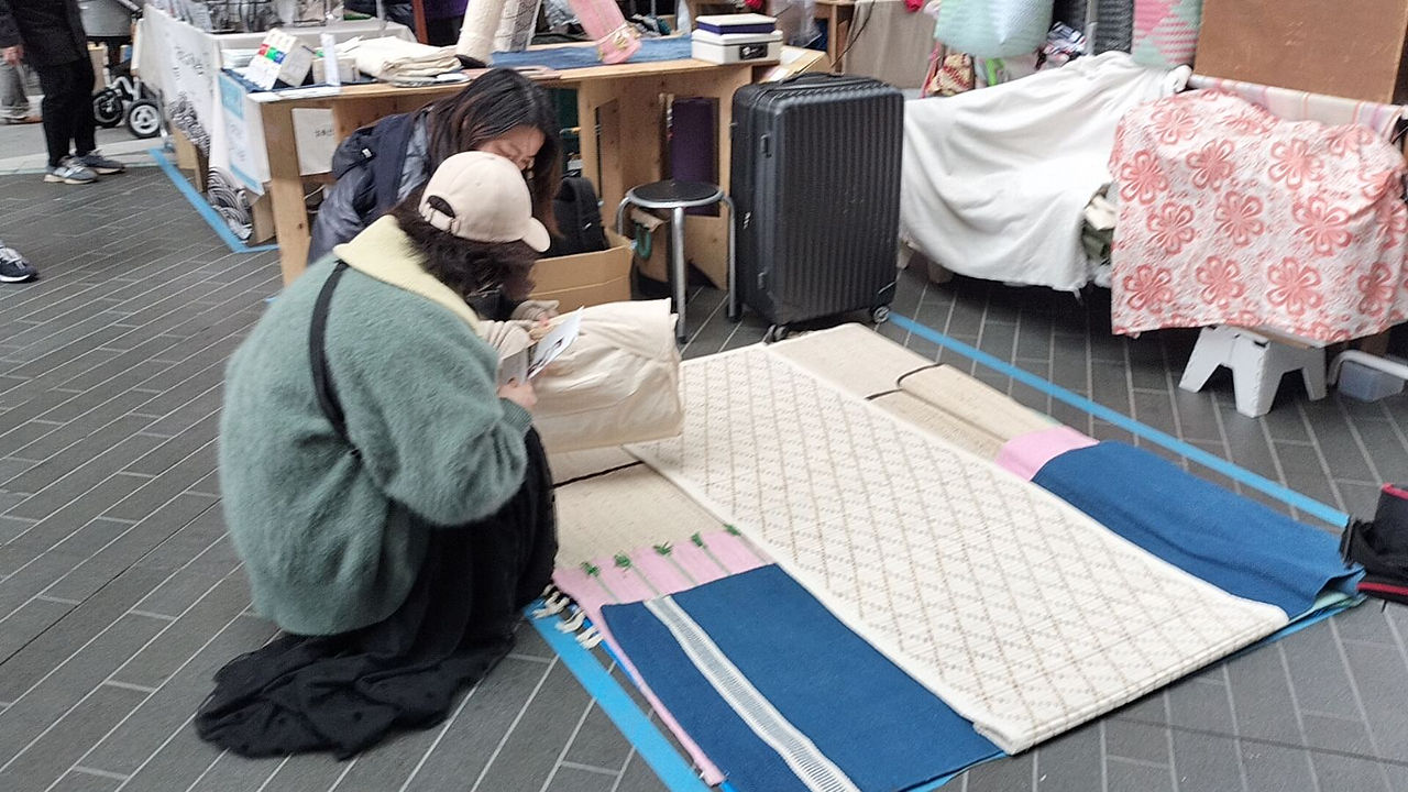 展示されたヨガラグの素材を手で確かめる来場者たち Visitors examining the material of natural yoga rugs on display