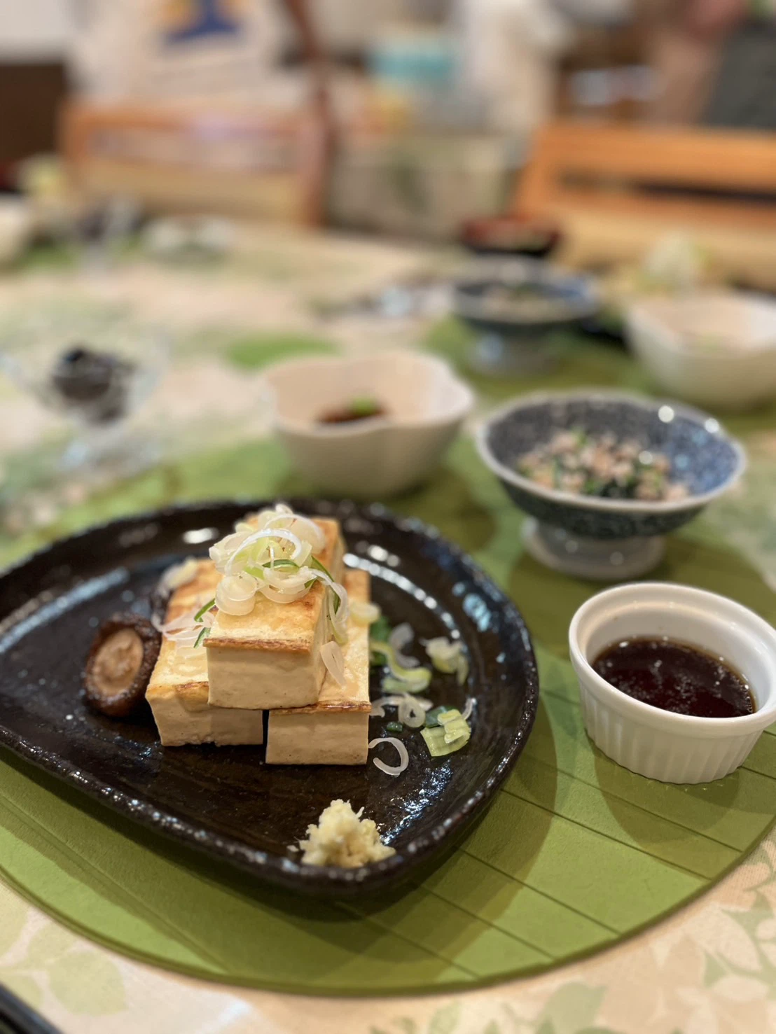青ねぎが乗った焼き豆腐。生姜とタレが添えられた一品です。
