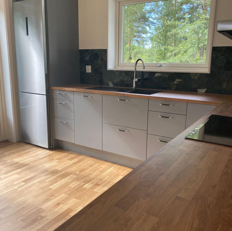 Nyrenoverat kök med minimalistisk design, gråa skåp, bänkskiva i trä och integrerade moderna vitvaror, som skapar en elegant och funktionell matlagningsmiljö. Åkersberga, Bromma, Spånga