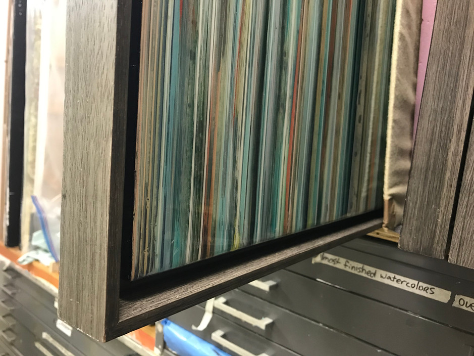 Framed works are permanently attached inside brownish grey wood floater frames.