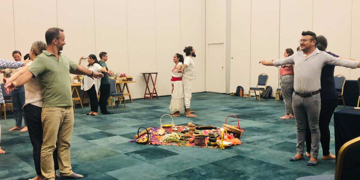 A team in a wide circle with their arms stretched out, around an altar of flowers and fruit
