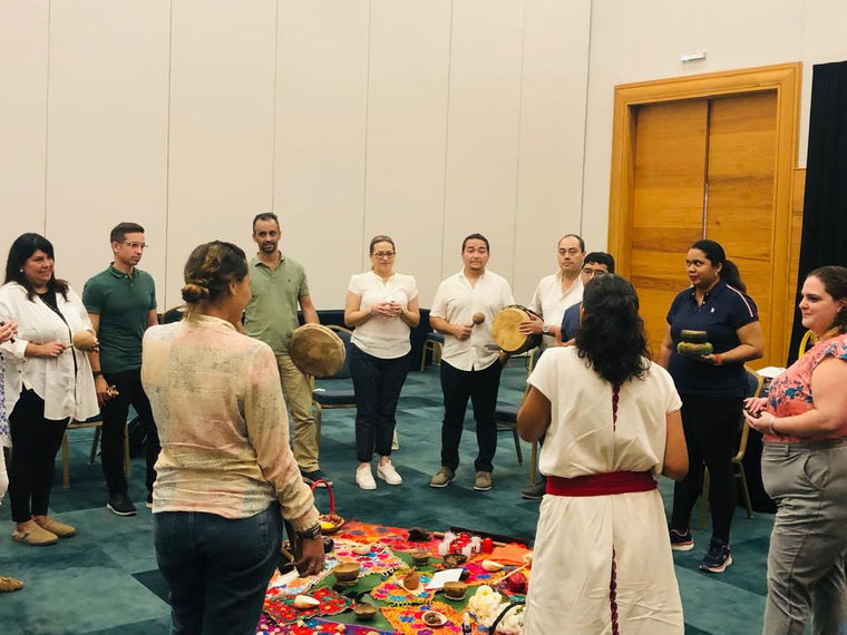 A team standing in a circle with the Mayan guides, who hold drums