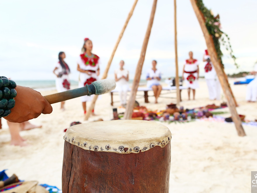 Tambor en primer plano y personas vestidas de blanco durante una ceremonia en la playa