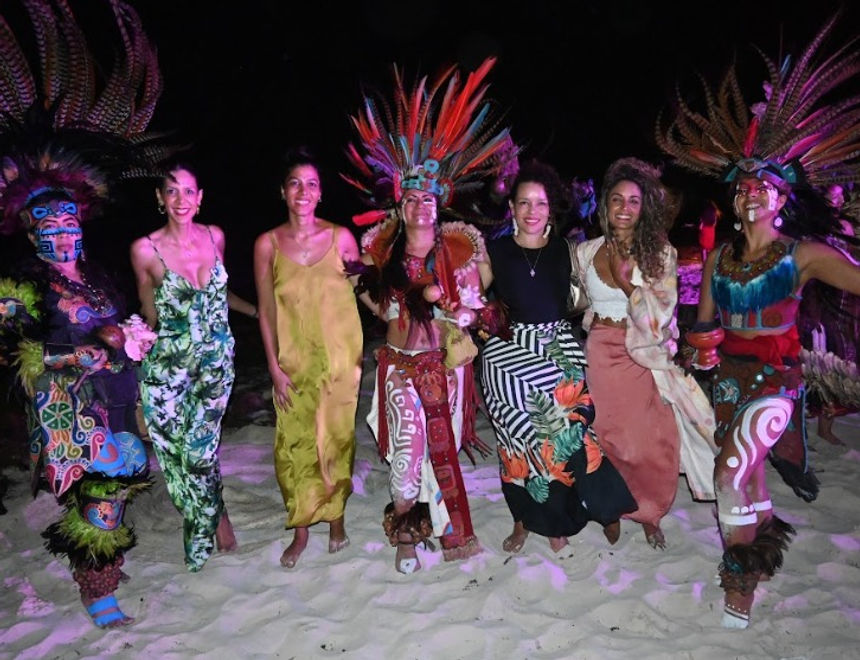 Guests dancing on the beach at night alongside dancers in feathered headdresses