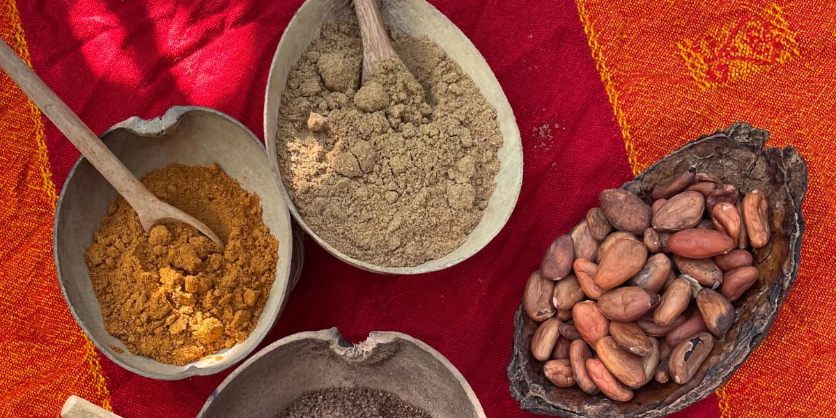 Cacao beans in a wooden bowl and ground ingredients in clay bowls on a red embroidered cloth