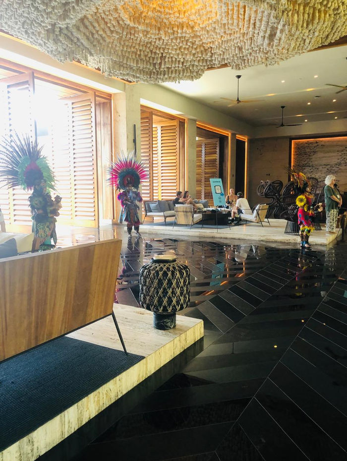Three dancers in feathered headdresses waiting in a hotel lobby before the welcome