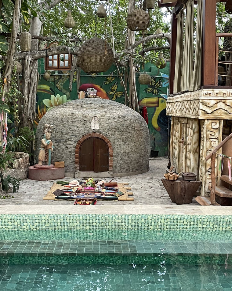 Temazcal de piedra con el altar montado delante y una alberca de mosaico en primer plano