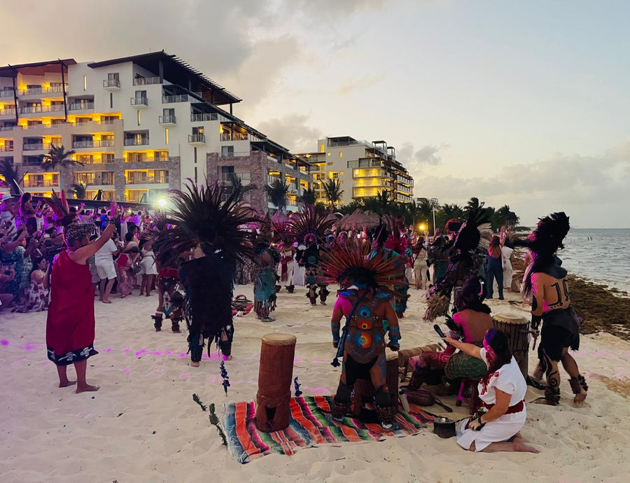 Dancers and drums on the beach at dusk, with the group standing in a circle around them