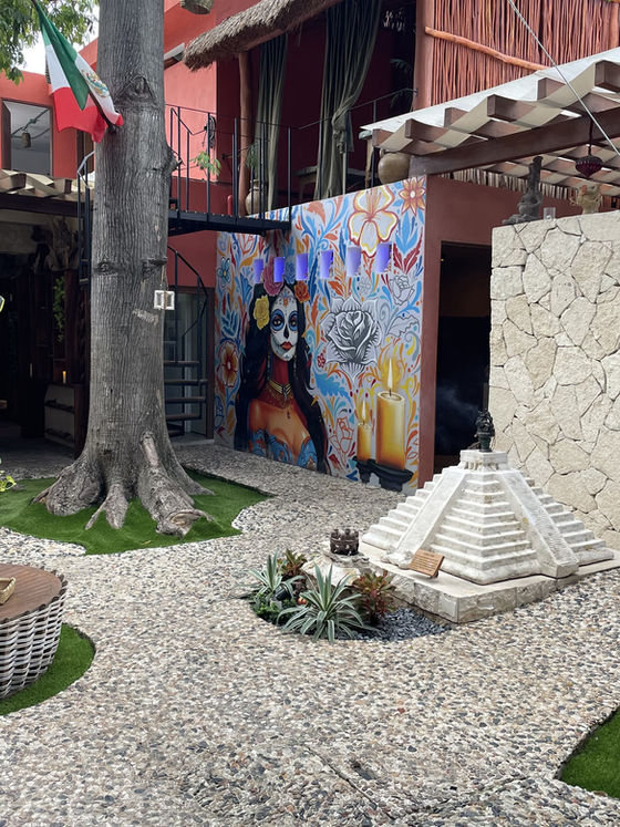 Patio con un mural pintado, una pequeña pirámide de piedra y suelo de canto rodado