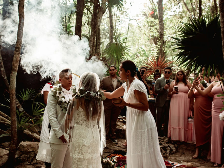 Un guía espiritual rodea a una pareja con humo sagrado en la selva, con sus invitados detrás