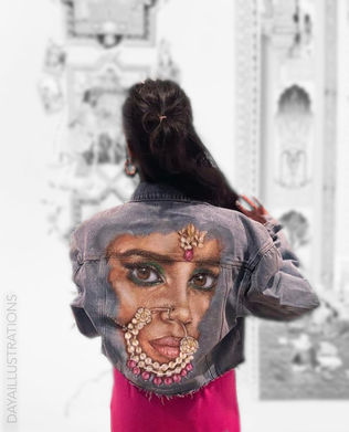 Figure wearing a denim jacket featuring a painted portrait of a South Asian woman with a traditional nose ring.