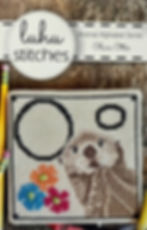 Cute cross-stitched otter holding flowers in a square border with large stitched letter O.