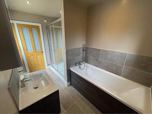 Modern bathroom featuring tiled walls, white bathtub, vanity unit and glass shower enclosure