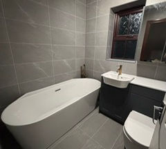 Modern bathroom with grey wall tiles, freestanding bathtub, dark vanity unit and toilet