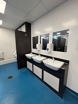 Modern commercial washroom with multiple white basins and dark toilet cubicles