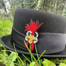 Haut de forme feutre, cravate satin noir et sa broche poule à crête