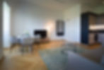 Bright living and dining area with sofa, coffee table and dining table as well as modern kitchenette in the PREMIUM SUITE N°307 in the Erlenbad Resort, with parquet flooring, high ceilings and large windows for plenty of daylight.