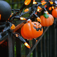 String of small plastic jack-o-lanterns and Halloween fairy lights strung on a black wrought iron fence. Image by John Hayler on Unsplash.