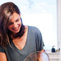 Two women with dark hair laugh together as they prepare food in the kitchen. Image courtesy of Two Alpha Gals.