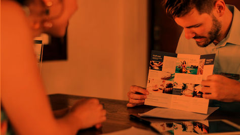 A hotel staff member showing a personalized brochure with wellness and activity options to a guest at the front desk, highlighting tailored hospitality services.
