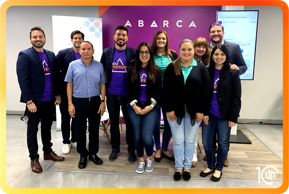 Group photo of DuartePino and Abarca Health team members smiling at the camera during an in-office event. Some individuals wear purple “PBM AWESOME” t-shirts, while others wear business or branded attire. The purple Abarca logo appears in the background. The image is framed with DuartePino’s 10th anniversary branding and the “10DP” logo in the corner.