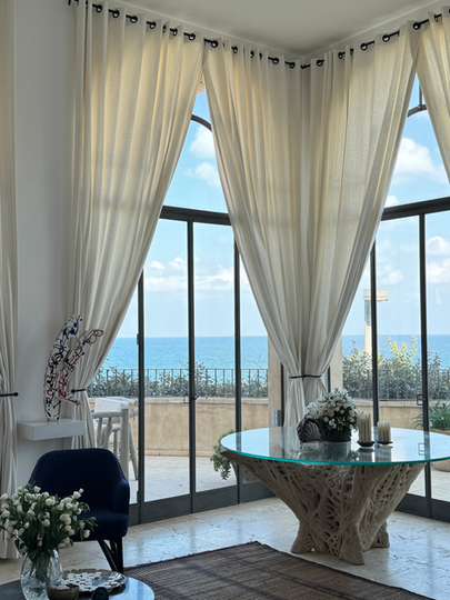 Elegant room with sheer curtains, blue sea view, round table, and flowers.