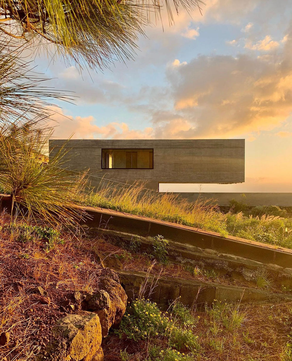 x Esta vivienda unifamiliar, construida en hormigón armado, redefine la experiencia de habitar el espacio al elevar literalmente parte de su volumen. La mitad de la casa parece flotar sobre el jardín y la terraza, generando una sensación de ligereza y libertad que contrasta con la solidez del material. Esta disposición no solo crea vistas panorámicas y una conexión directa con el entorno, sino que también permite que la luz y el aire circulen de manera natural bajo el volumen suspendido. Cada detalle refuerza la idea de un hogar moderno que desafía la gravedad y combina funcionalidad, confort y una poética relación con la naturaleza circundante.