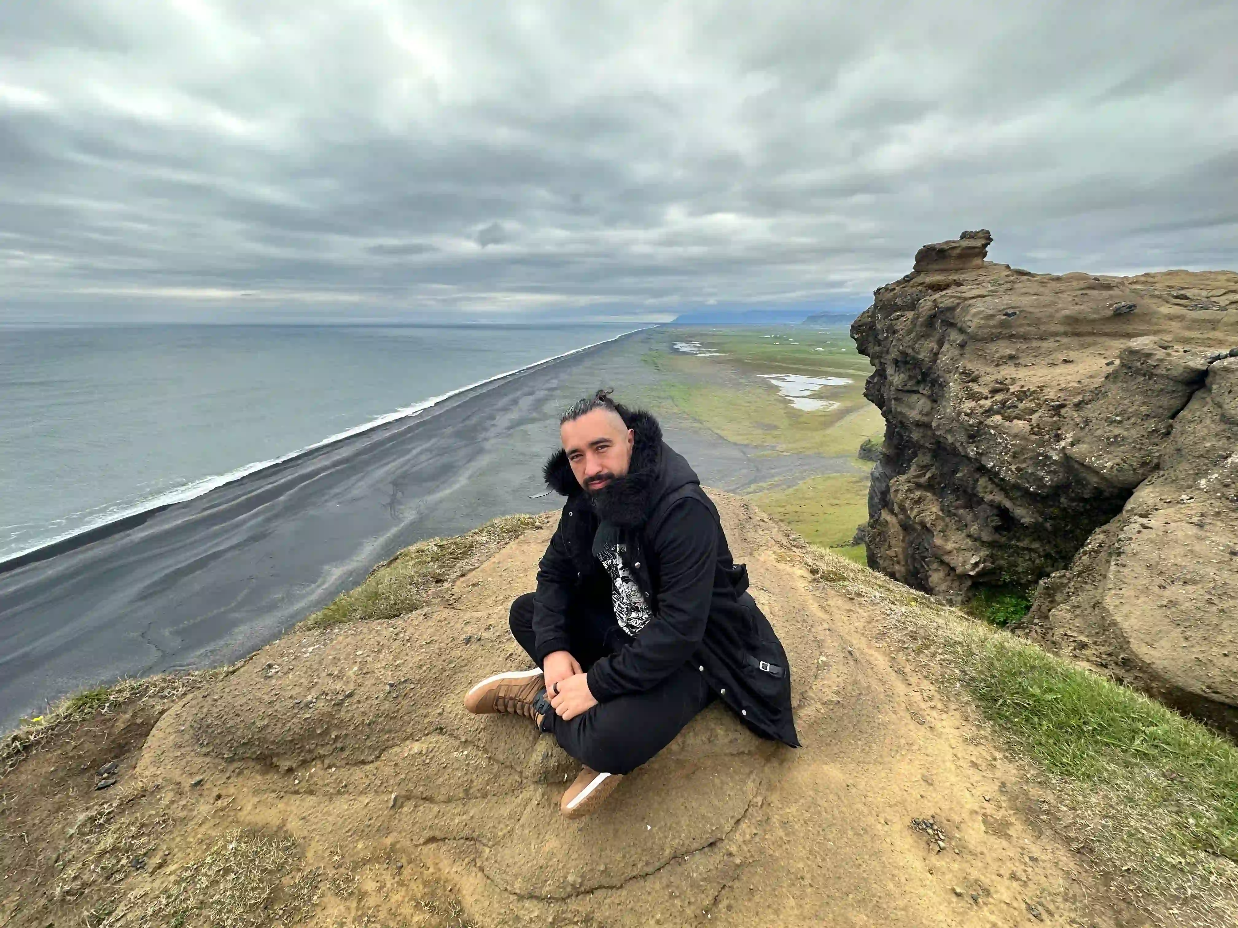 A man seating on the edge of a rock at Dyrholaey view point, as part of the South Coast Pr