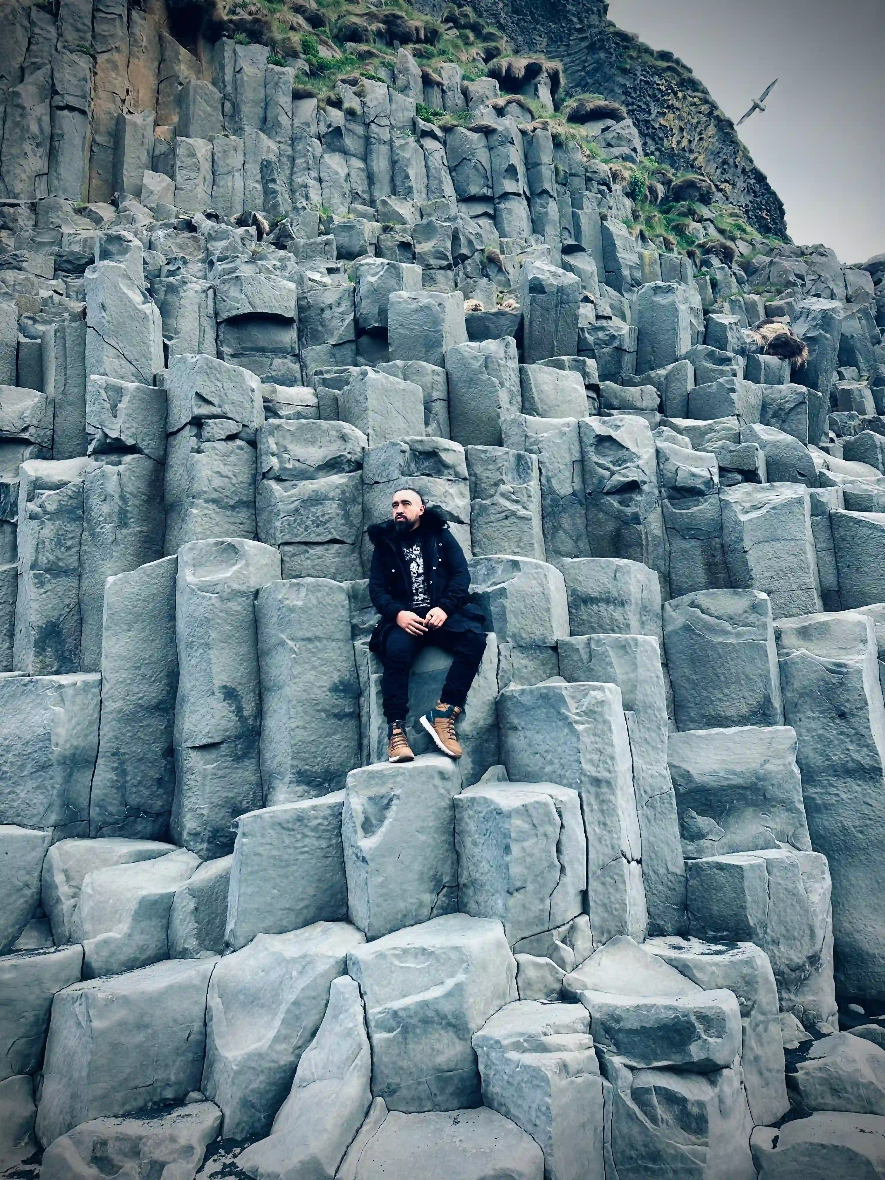 A man seating on the basalic rock formations at Reynisfjara Black beach, part of the South