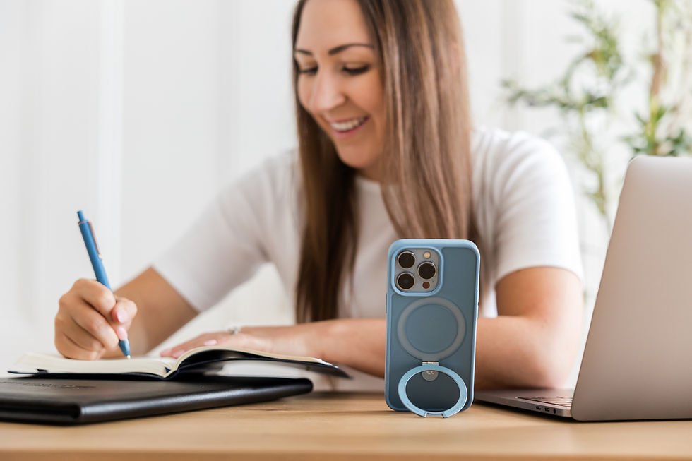 Woman writing in notebook at desk with phone and laptop