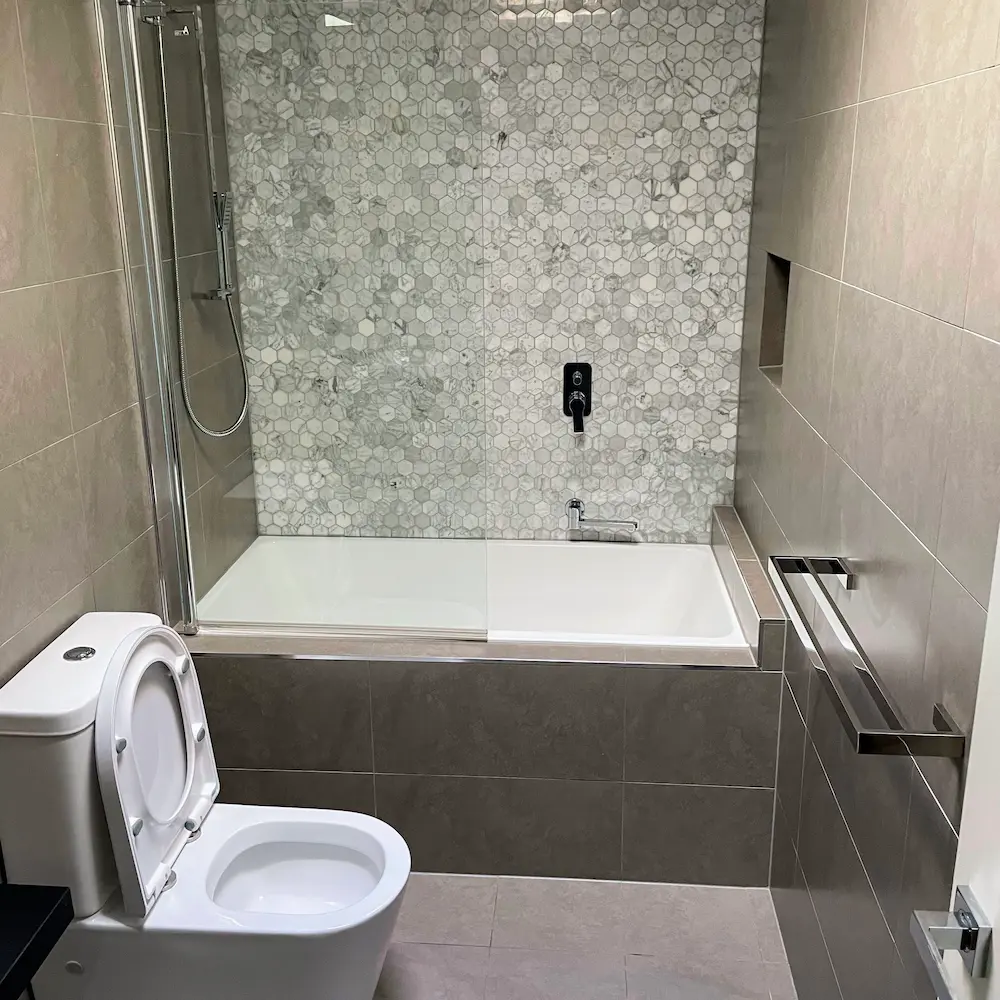 Modern bathroom suite featuring white marble hexagon feature tiles, descaled bathtub glass screen, and sanitised toilet detailed by Whole Detail. 