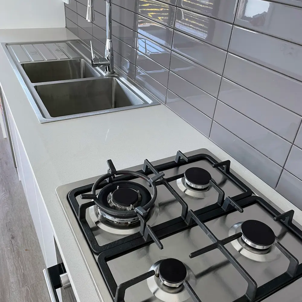 Four-burner gas cooktop, double bowl sink, and grey subway tile splashback degreased and detailed by Whole Detail. 