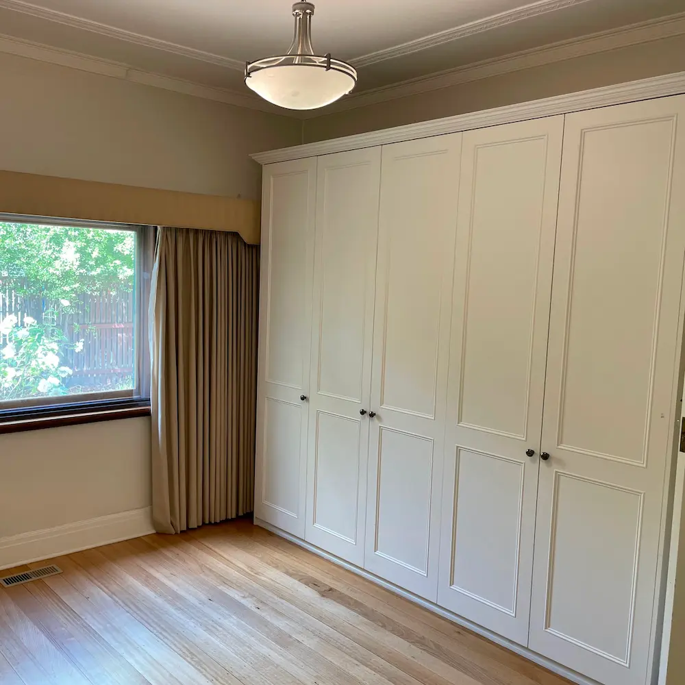 Full-height white built-in wardrobe joinery, ceiling light fixture, and window sills detailed during residential spring cleaning. 