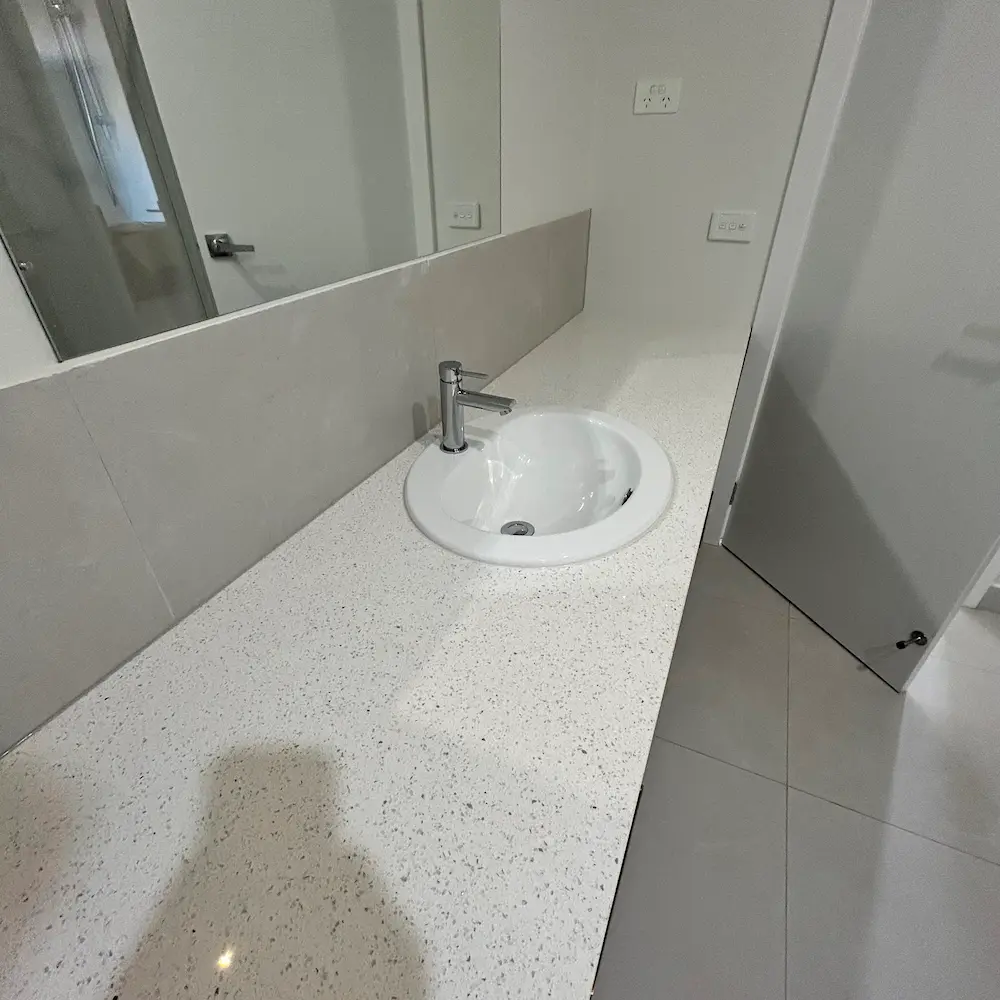 White stone vanity countertop, undermount ceramic basin, and polished tile floor detailed by Whole Detail. 