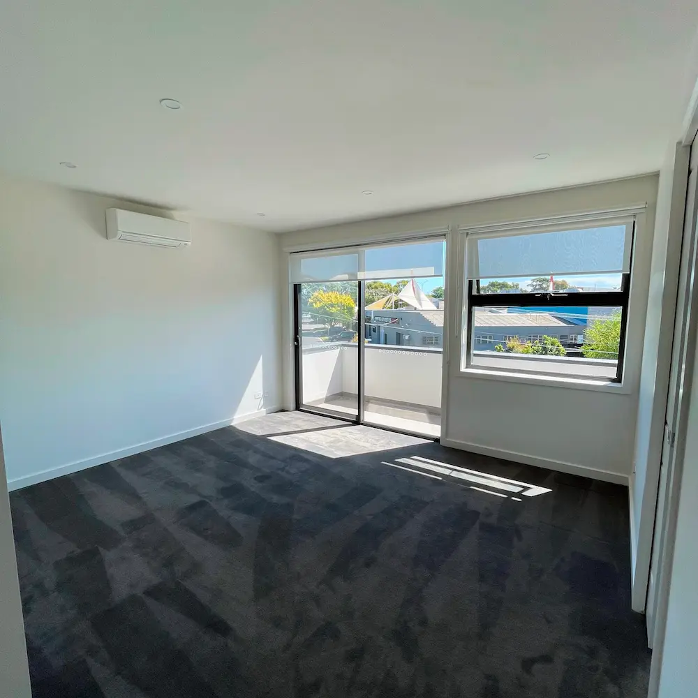 Spacious master bedroom featuring HEPA-13 vacuumed dark carpet, wall-mounted split system air conditioner, and detailed sliding glass doors. 