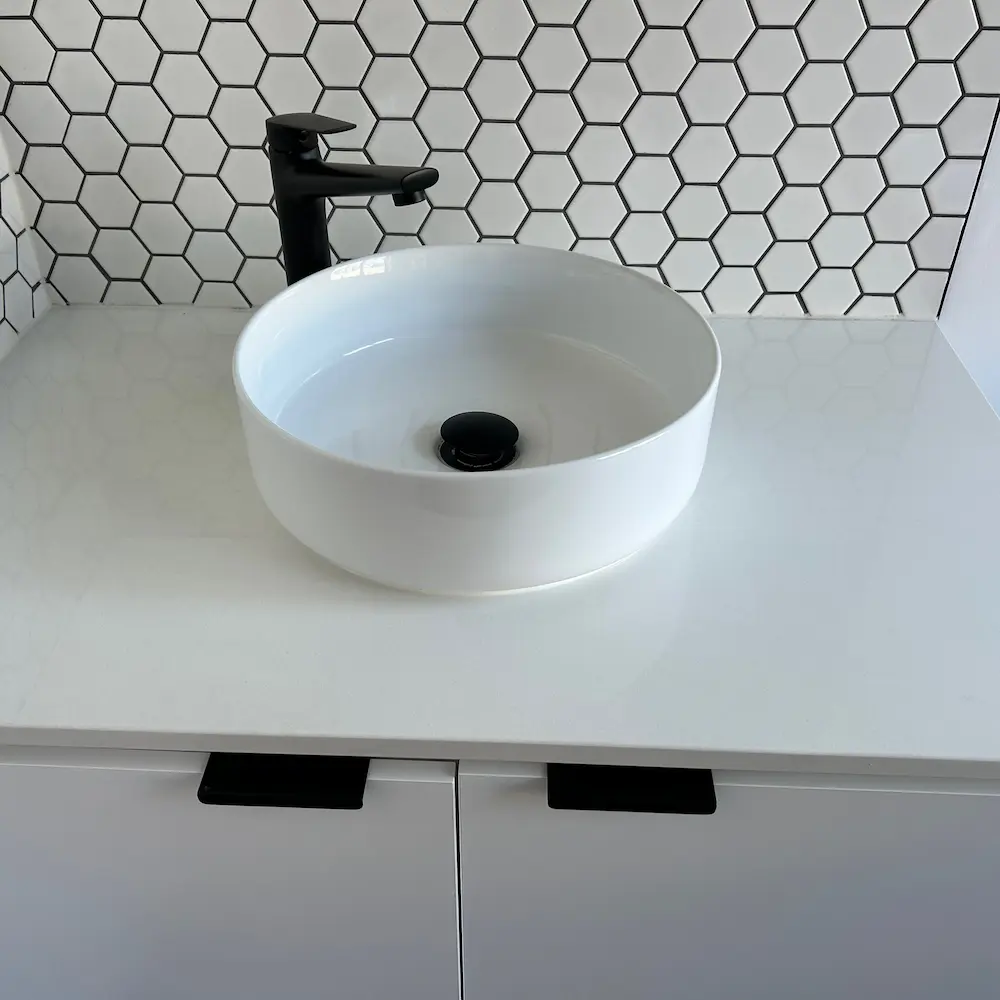 Above-counter ceramic basin, matte black tapware, and white hexagon splashback tiles detailed by Whole Detail. 