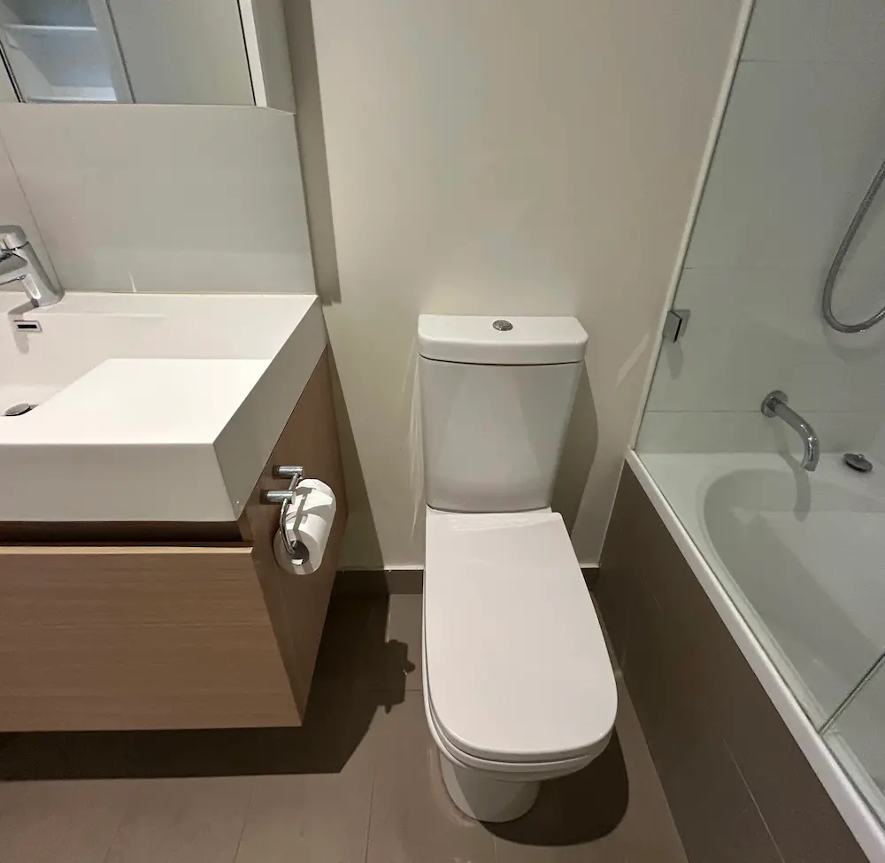 Deep cleaned apartment bathroom including descaled glass shower screen, sanitized vanity, and ceramic toilet by Whole Detail. 