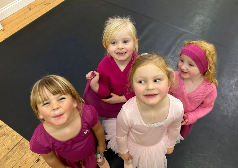 Picture of a group of preschool children, dressed in dance uniform, all smiling up at the camera.