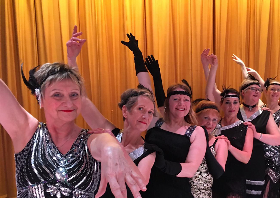 Picture of adult tap dancers in black and silver flapper dresses all smiling and posing for the camera.