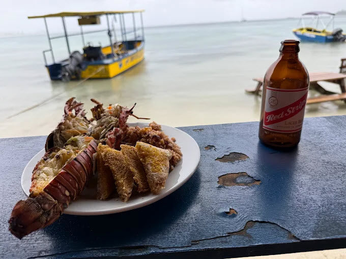 Lobster meal served beside the Caribbean Sea with a boat in the background