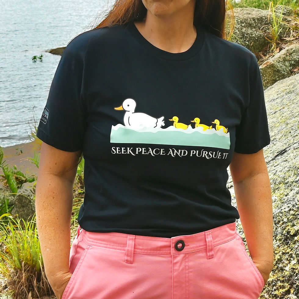 Woman in black t-shirt, duck family graphic, "SEEK PEACE AND PURSUE IT".