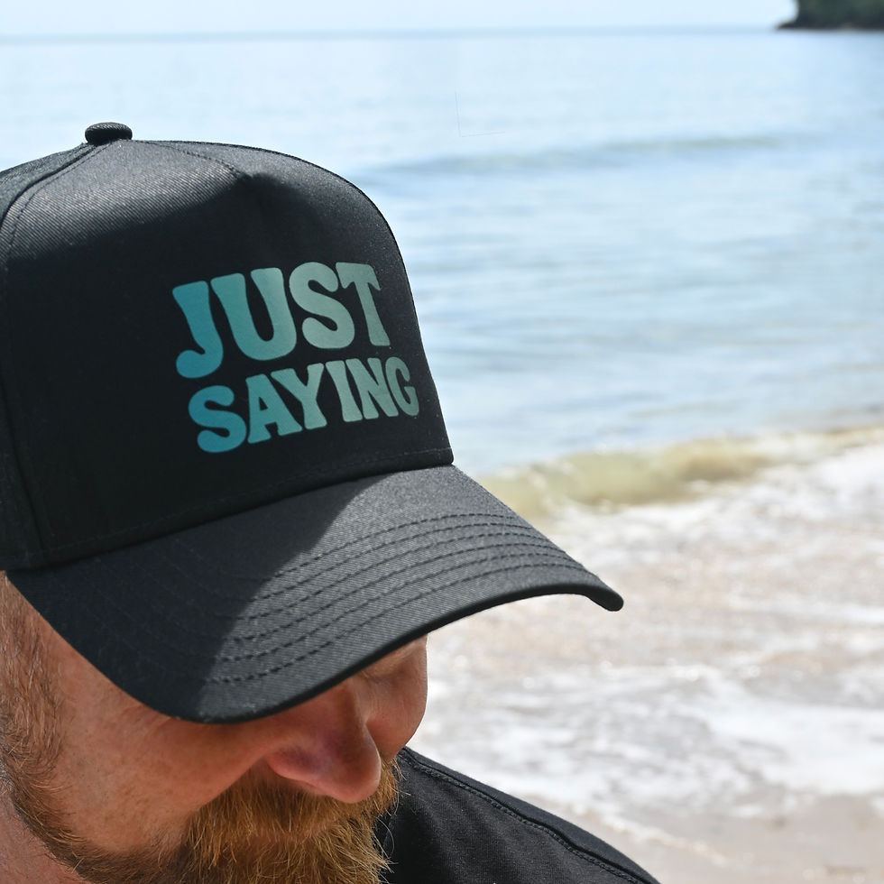 Man wearing black cap with 'JUST SAYING' text, ocean background.