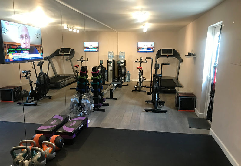 Gym shot towards cardio end - equipment depicted includes rowing machine, treadmill, spin bike, air bike, free weights and kettlebells.