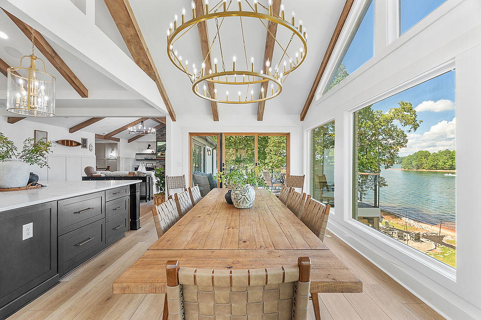 Bright, modern dining room with wood beams, large chandelier, long wood table, and big windows overlooking a lake, wide landscape orientation.