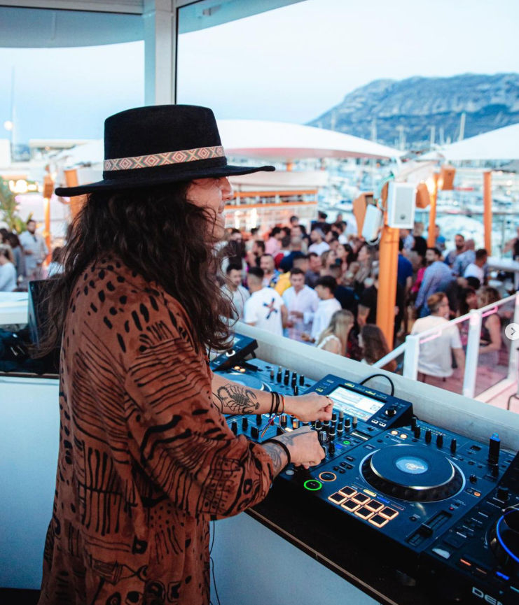 Un DJ pincha en Lamarserena mientras la gente disfruta del atardecer y de la fiesta durante su estancia de fin de semana en Denia's Dream.