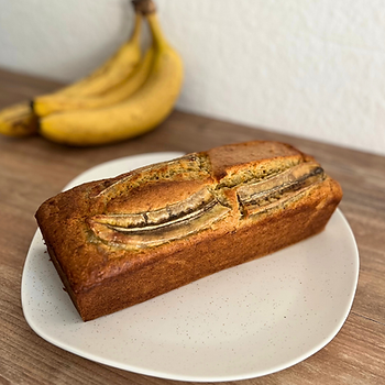 Bananenbrot auf einem weißen Teller mit einer Staude Bananen im Hintergrund