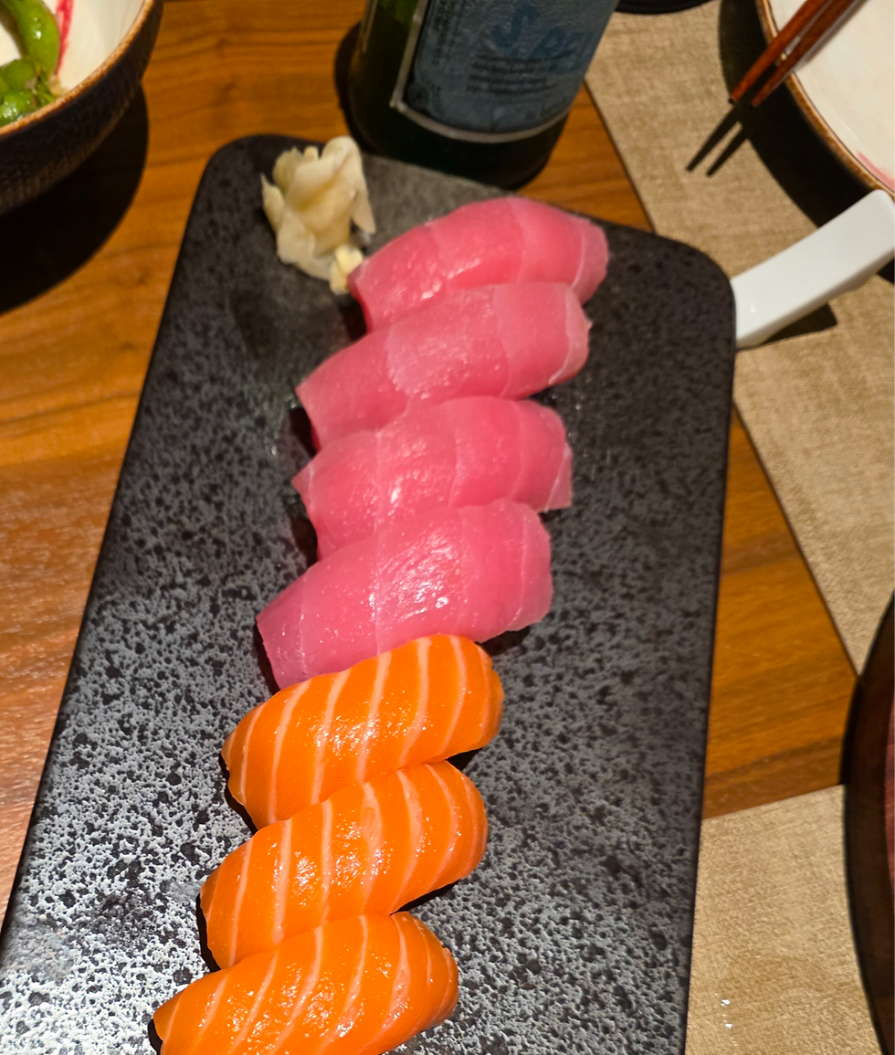 Sushi plate with pink tuna and orange salmon sashimi on black slate. Wooden table and chopsticks in the background.