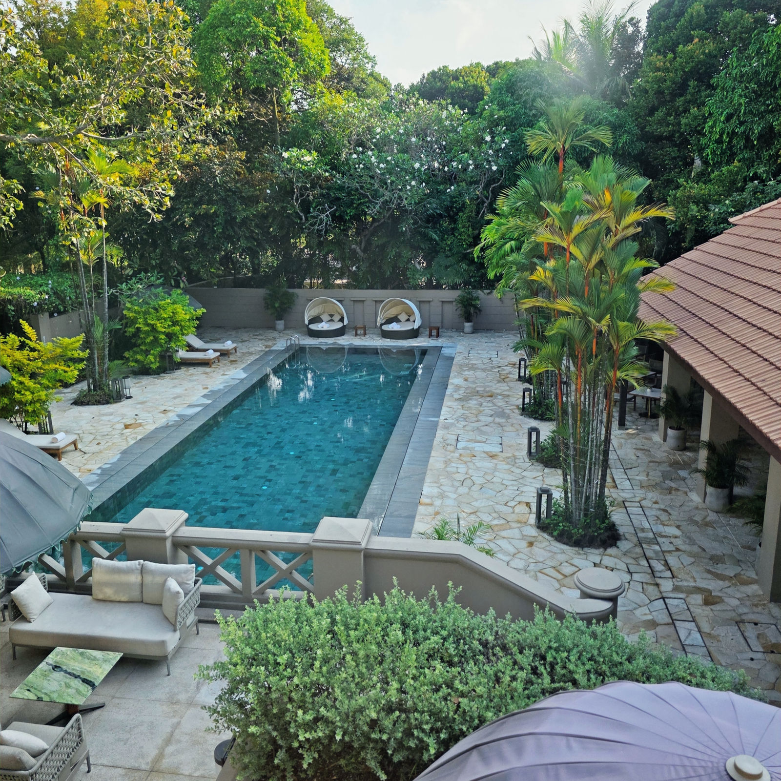 Elegant pool area surrounded by lush greenery, stone patio, and luxurious seating. Clear blue water reflects the serene, tropical atmosphere.