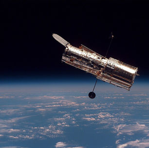 A long, tube-shaped satellite floats in space over Earth.