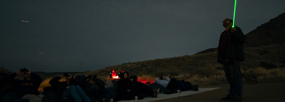 A stargazing tour. Guests are looking up as a guide uses a laser pointer